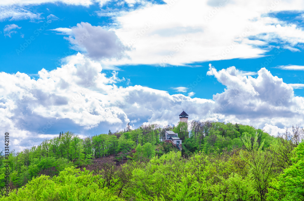 Diana Observation Tower (Rozhledna Diana) and funicular on hill above Slavkov Forest with green trees and Karlovy Vary (Carlsbad) town, blue sky white clouds background, West Bohemia, Czech Republic