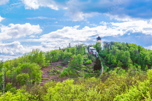 Diana Observation Tower (Rozhledna Diana) and funicular on hill above Slavkov Forest with green trees and Karlovy Vary (Carlsbad) town, blue sky white clouds background, West Bohemia, Czech Republic photo