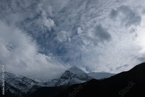 Snowy mountain range in clouds and sun - Annapurna massif around Manang. Himalaya, Nepal. During trekking around Annapurna. photo