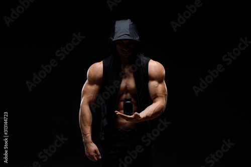 Muscular bodybuilder with jar of protein on a dark background. Sports nutrition. Bodybuilding nutrition supplements, sport, workout, healthy lifestyle concept.
