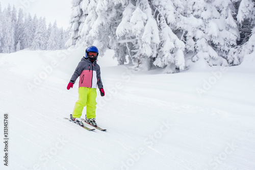 Child in ski suit skiing downhill in mountains during winter season