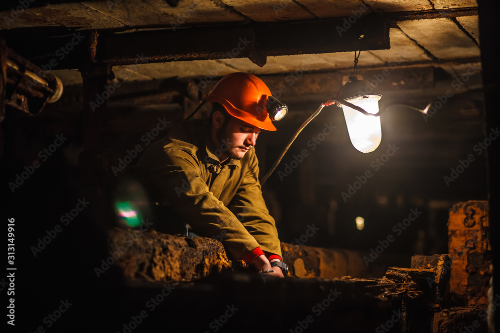 A tired miner in a coal mine looks at the light. Work in a coal mine. Portrait of a miner. Copy space.