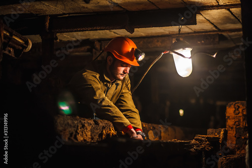 A tired miner in a coal mine looks at the light. Work in a coal mine. Portrait of a miner. Copy space. photo