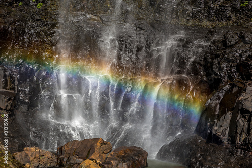 Small colourful rainbow fills a rock filled small waterfall