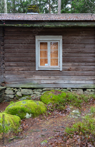 Window of an ancient authentic wooden house of the 17th century near large stones in a forest on the island of Seurasaari in Helsinki, Finland, a cloudy day in late autumn. The harsh beauty of ancient