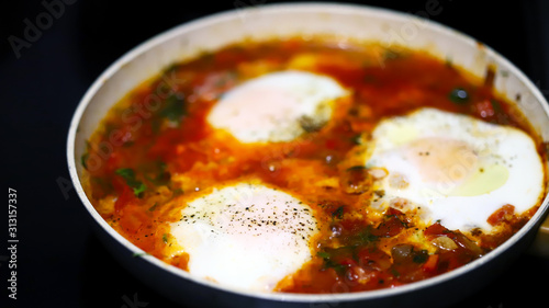 Selective focus. Shakshuka cooked on a frying pan. Cooking Israeli Shakshuka fried eggs. Middle Eastern cuisine. Fried eggs in tomato sauce.