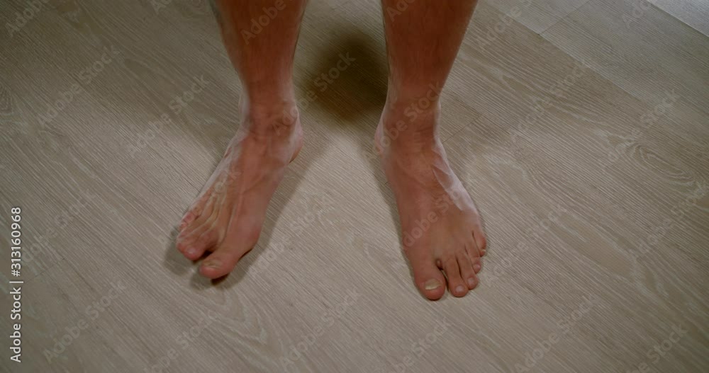 bare man is standing on floor in living room, closeup view on his legs and feet bare man is standing on floor in living room, closeup view on his legs and feet
