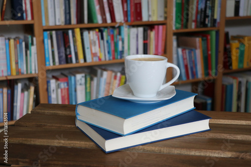 Kaffee, Cappuccino in Tasse mit Buch vor Bücherregal