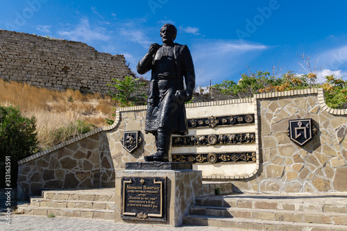 Feodosia, Crimea, Russia - September 26, 2019: Sculpture of travel writer Athanasius Nikitin on Genoese fort background. photo