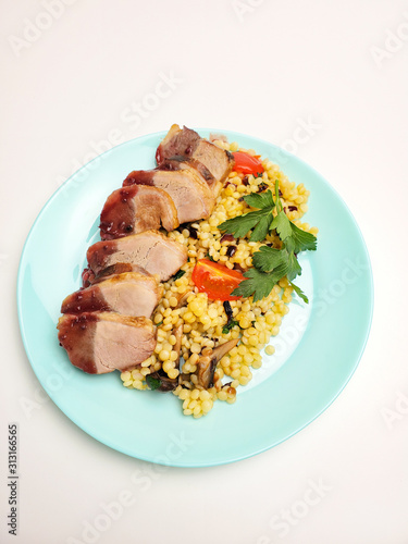 Duck breast fillet with garnish and sauce on a plate on a white background.