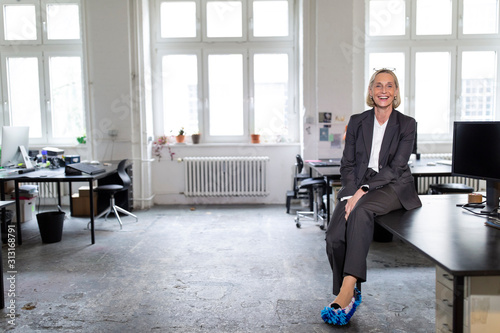 Happy mature businesswoman wearing cleansing slippers in office photo