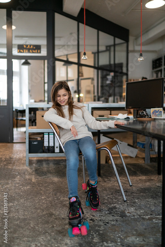 Girl with roller skates sitting at desk in office wobbling with chair