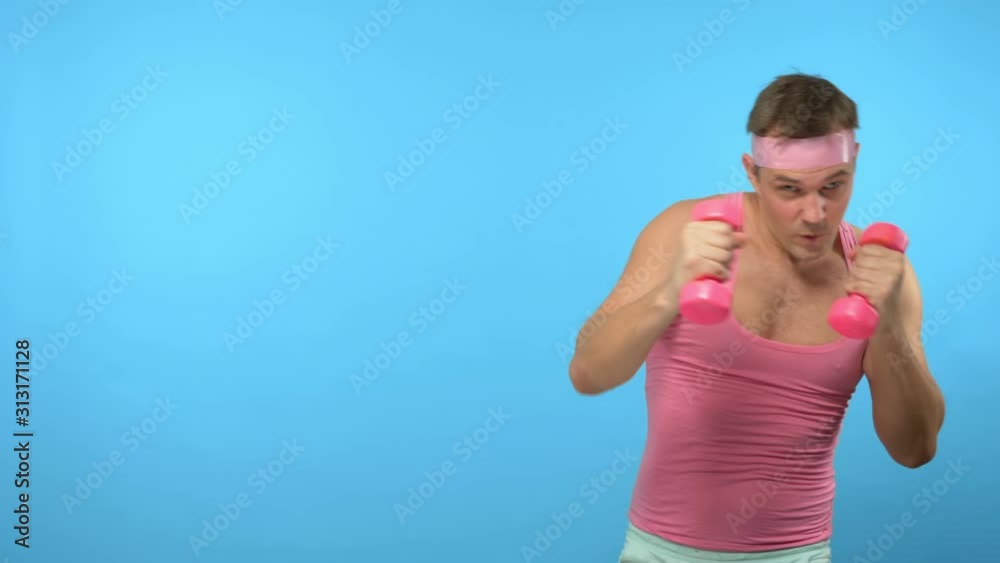 Playful handsome man in a pink t-shirt is engaged in fitness in pink glasses with pink dumbbells. Bright Fitness. Sports Fashion Accessories Playful handsome man in a pink t-shirt is engaged in fitness in pink glasses with pink dumbbells. Bright Fitness. Sports Fashion Accessories