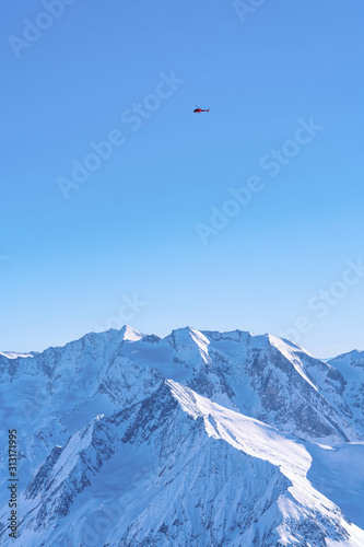 Aerial view of Helicopter flying over Hintertux Glacier in Tyrol in Mayrhofen in Zillertal valley of Austria in winter Alps. Chopper above Peaks of Hintertuxer Gletscher in Alpine mountains. Blue sky