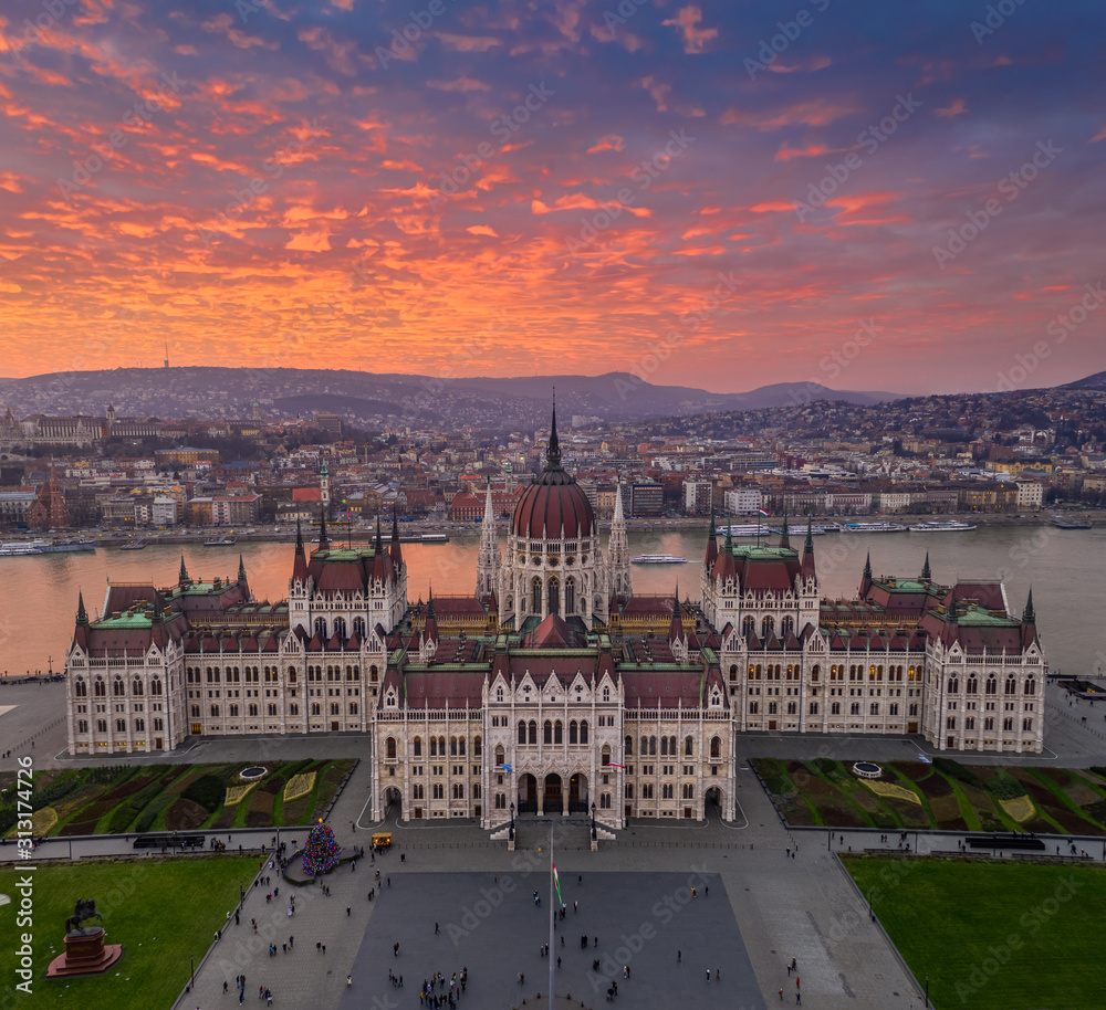 Budapest, Hungary - Aerial panoramic drone view of the Parliament of Hungary at sunset with beautiful dramatic purple clouds, Christmas tree and sightseeing boats on River Danube