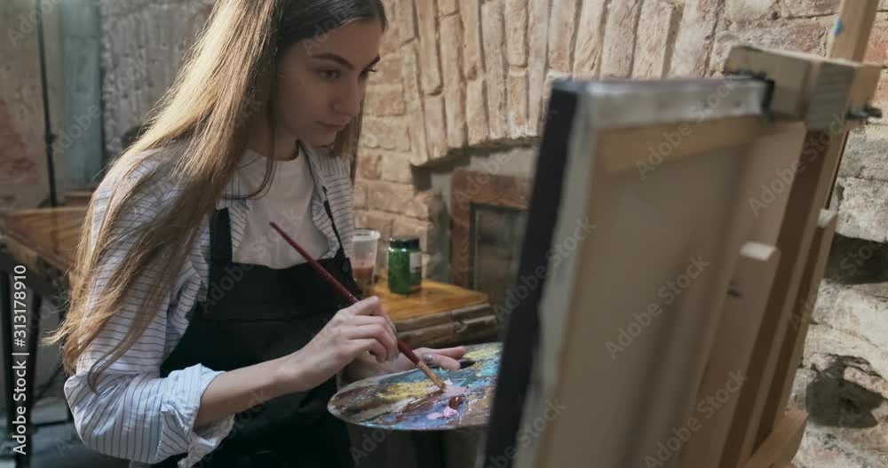 Talented innovative pretty Female Artist Draws with brush on the Canvas. Contemporary young woman painter creating abstract picture. Attractive girl creates modern art painting Talented innovative pretty Female Artist Draws with brush on the Canvas. Contemporary young woman painter creating abstract picture. Attractive girl creates modern art painting