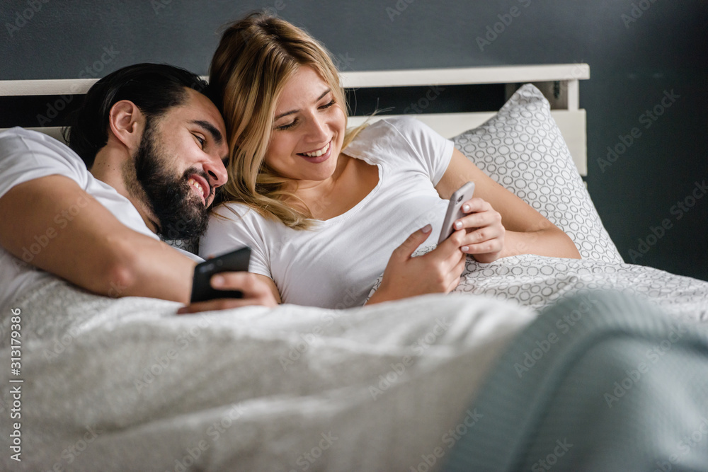 Young adult couple using smartphones in the bed addicted to social networking. Mobile addiction concept Young adult couple using smartphones in the bed addicted to social networking. Mobile addiction concept