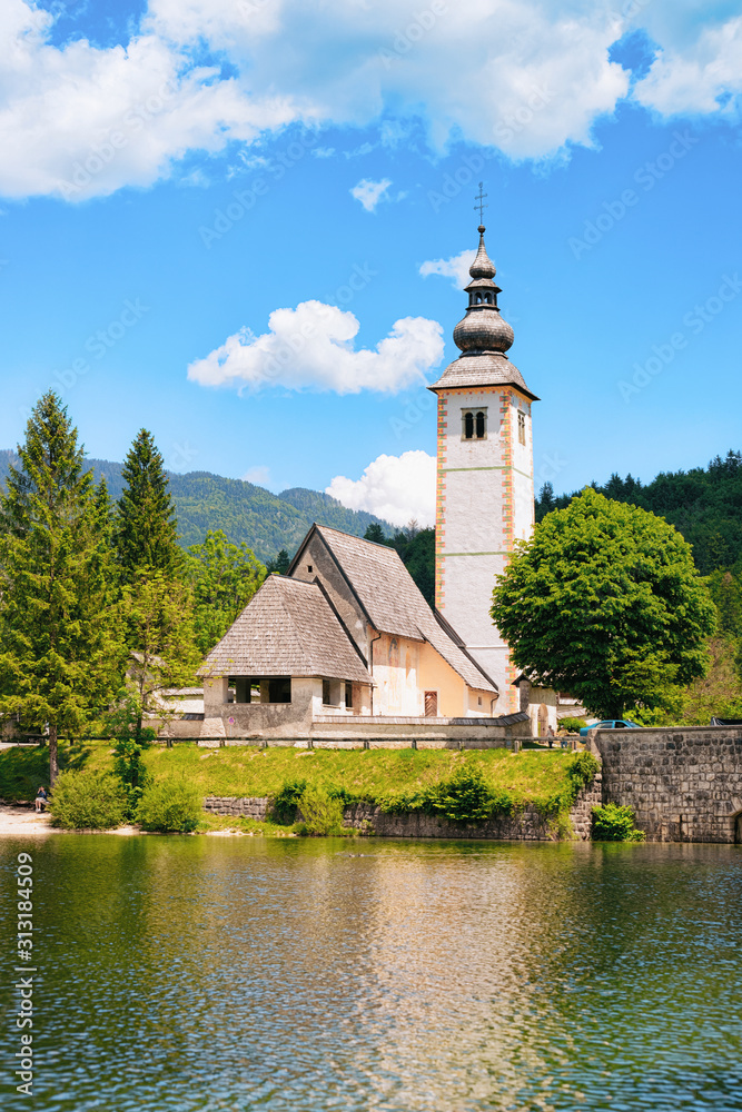 Scenery and Church of St John Baptist on Bohinj Lake, Slovenia. Nature in Slovenija. View of blue sky with clouds. Beautiful landscape in summer. Alpine Travel destination. Julian Alps mountains