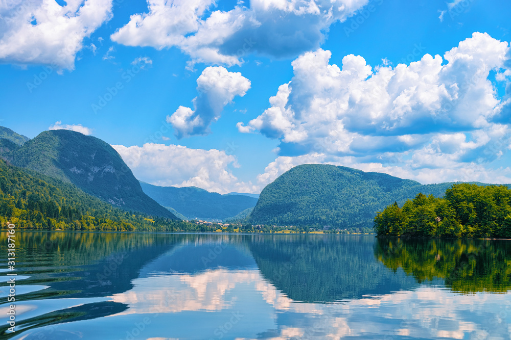 Scenery at Bohinj Lake in Slovenia. Nature in Slovenija. View of green forest and blue water. Beautiful landscape in summer. Alpine Travel destination. Julian Alps mountains on scenic background