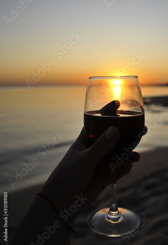 Wine glasses with red wine in female hand on the sunset beach. Valentine's Day concept.