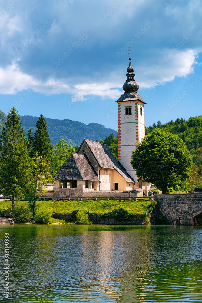 Scenery of Church of St John Baptist on Bohinj Lake in Slovenia. Nature in Slovenija. View of blue sky with clouds. Beautiful landscape in summer. Alpine Travel destination. Julian Alps mountains
