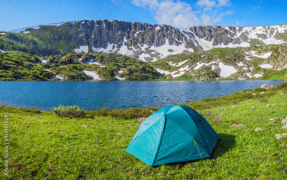 Summer holidays in the mountains, a tent on the shore of a mountain lake. Sunny day, bright landscape.