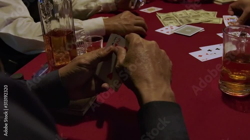 The cowboy's hands play cards on the table has a Dollar bills whisky bottles glasses of whisky  .
