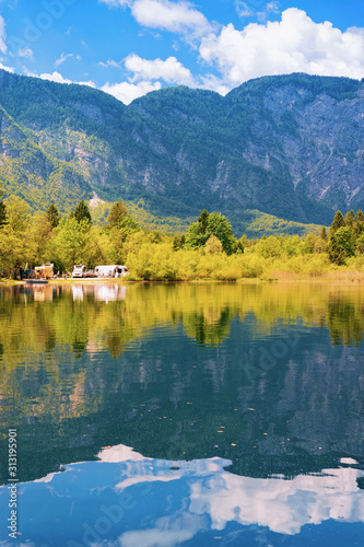 Scenery with camping of RV caravan trailers at Bohinj Lake of Slovenia. Nature and camper motorhomes in Slovenija. View of motor home van and green forest. Landscape in summer. Alpine Alps mountains