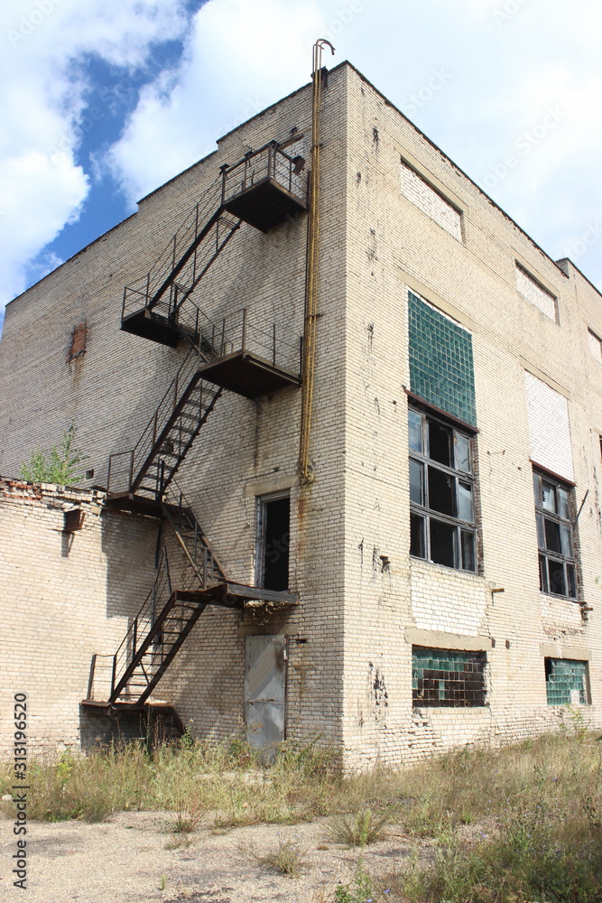 Abandoned factory house wall with outside rusty iron staircase, old industrial building outdoor view on sunny summer day