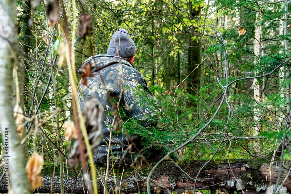 Obraz premium autumn hunter sits on log in a mixed forest, hunting and poaching, hunting for animals and game, opening hunting season