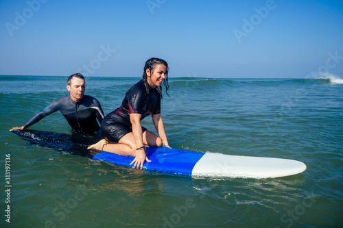 man instructor demonstrating how to stand up on surfboard to indian woman in surf class in Goa sea