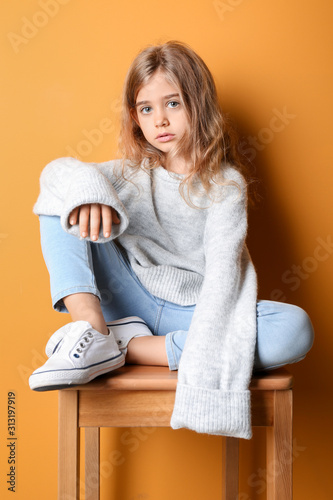 Cute fashionable girl sitting near color wall