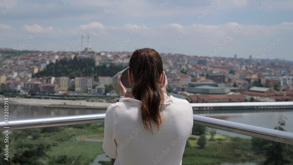 brunette woman in white sweater looks through binoculars exploring cityscape stretching along bay backside view
