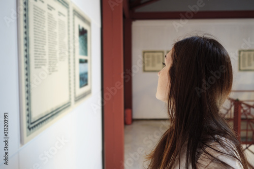 smart long haired girl spends leisure time in ancient museum and examines outstanding bass-reliefs hanging on wall closeup photo