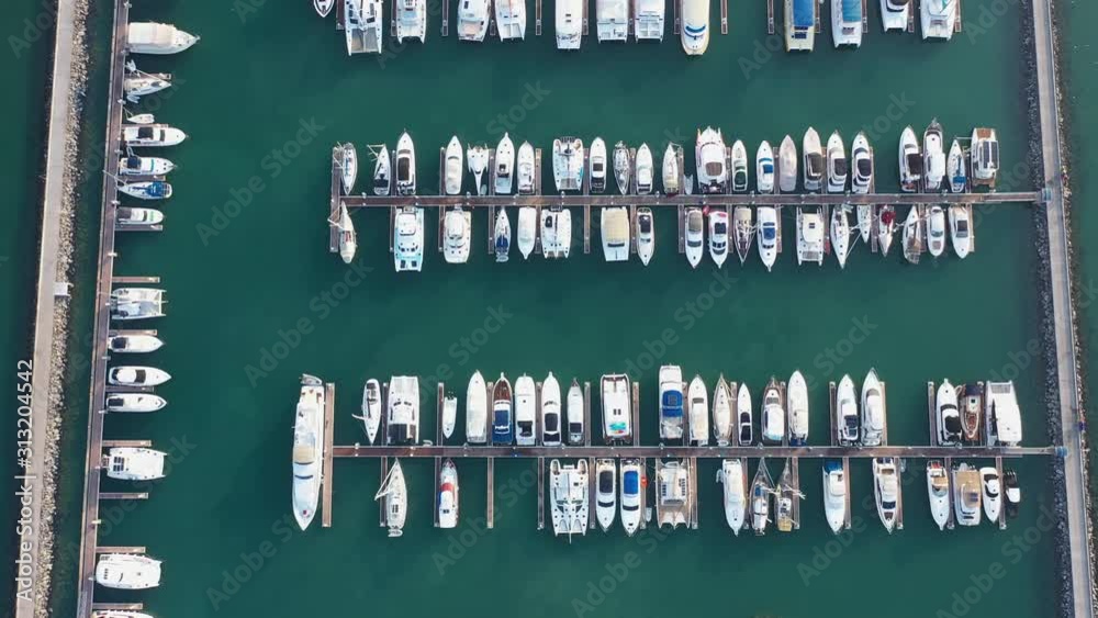 Aerial view of a white motor yacht. Yacht enters the bay in the parking lot. Many different yachts, catamarans moored to piers. Expensive yacht and travel place. Drone shot footage b roll scene 4K.