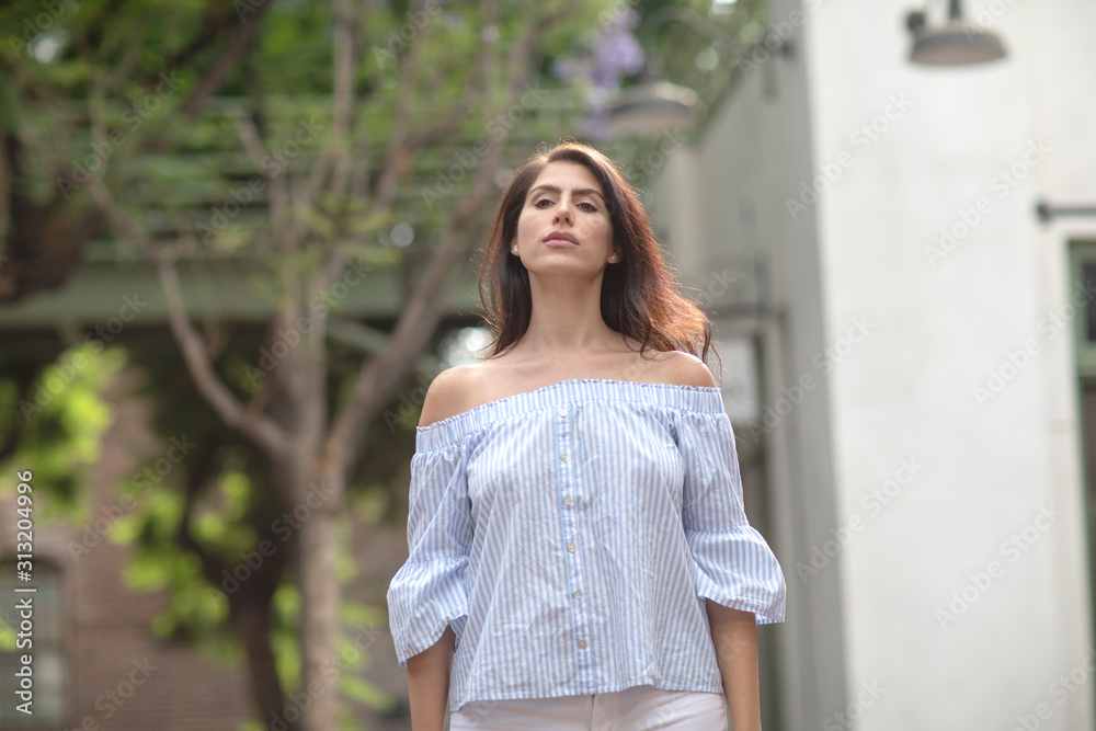 Beautiful young dark haired woman looking over her shoulder in a green street of a city Beautiful young dark haired woman looking over her shoulder in a green street of a city