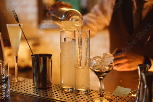 Bartender preparing a cocktail in a highball glass with crystal clear ice inside, at the bar counter. Selective focus, lifestyle horizontal photo