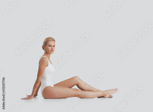 Young, beautiful, fit and natural blond woman in white swimsuit applying moisturizing cream. Massage, skin care, cellulite removal, sport and weight loss.