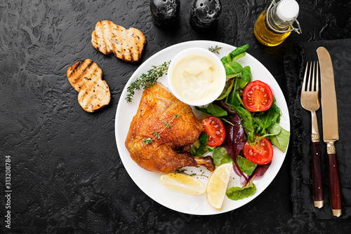 Baked chicken leg, served with sauce and fresh green salad. Black background