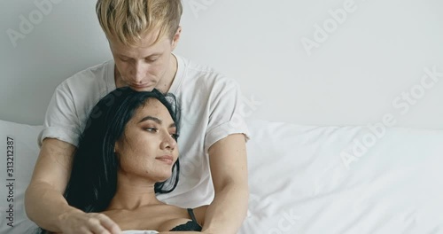 Lover sitting in bed thinking about future. Caucasian male with his girlfriend, asian woman in black lingerie. Happy lover in bed concept. photo