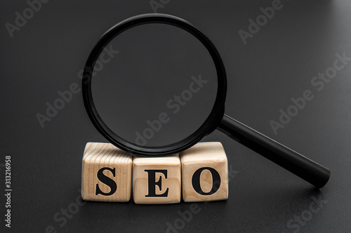 Wooden cubes with word "SEO" and magnifying glass on black.