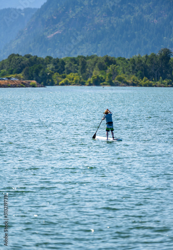  A man in a hat floats on the river standing with an oar on an inflatable board