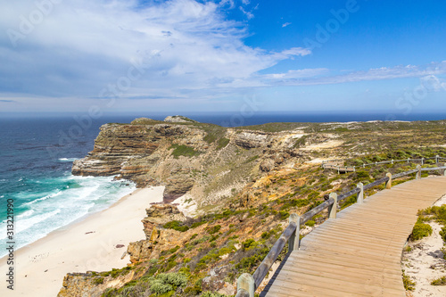Wooden walkway leading through fynbos vegetation with view to the ocean and Dias Beach on a sunny day, Cape of Good Hope, South Africa