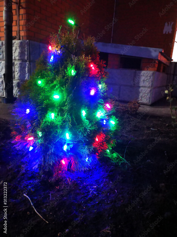 Fototapeta premium Christmas tree decorated with glittering toys shines beautifully with colorful lights in the dark