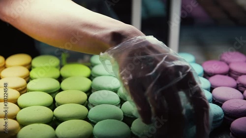 Closeup chef hand putting macarons at showcase. Colorful macarons at store glass photo