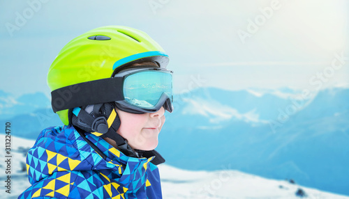 Boy in ski gear with goggles showing reflections of mountain peaks. Close-up, copy space beside