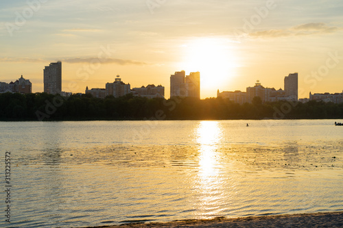 Beautiful view over the river bank at the sunset with cityscape at the background