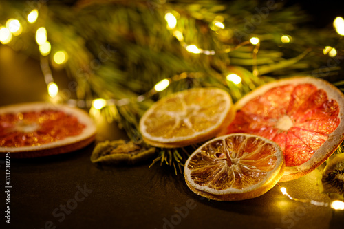 Creative moody holiday Christmas New Year food fruits with dried grapefruit  kiwi  orange and lemon with branch of fir tree with warm led lights  angle view  selective focus