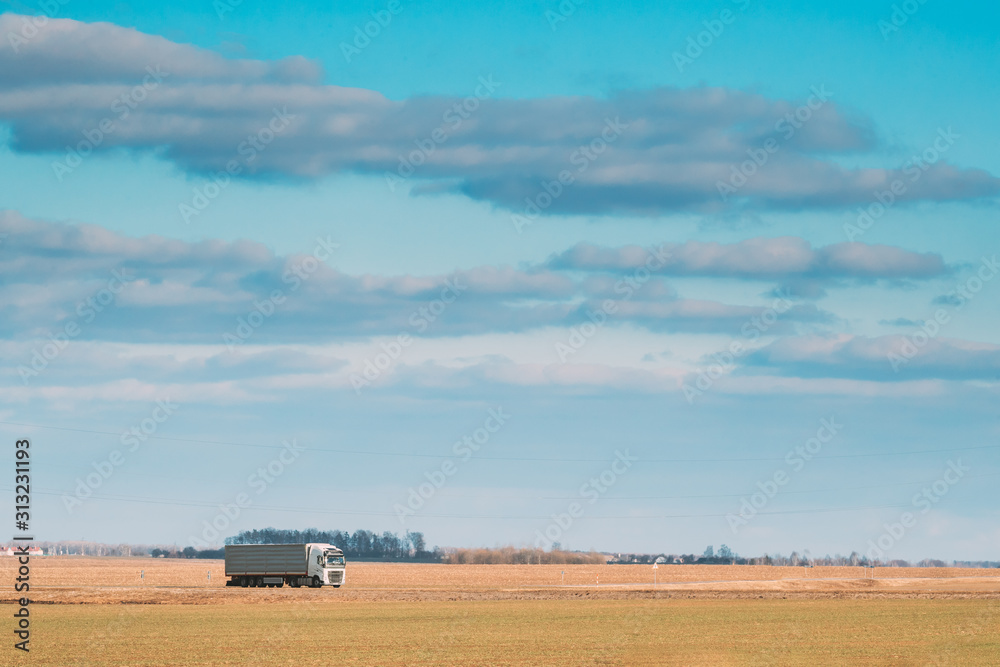 Truck Or Tractor Unit, Prime Mover, Traction Unit In Motion On Road, Freeway. Asphalt Motorway Highway Against Background Of Spring Meadow Field Landscape. Business Transportation And Trucking Truck Or Tractor Unit, Prime Mover, Traction Unit In Motion On Road, Freeway. Asphalt Motorway Highway Against Background Of Spring Meadow Field Landscape. Business Transportation And Trucking