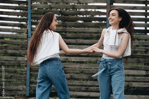 Portrait of Two Young Brunette Twins Sisters Dressed Alike in Jeans and White T-shirt  Best Friends Forever Concept